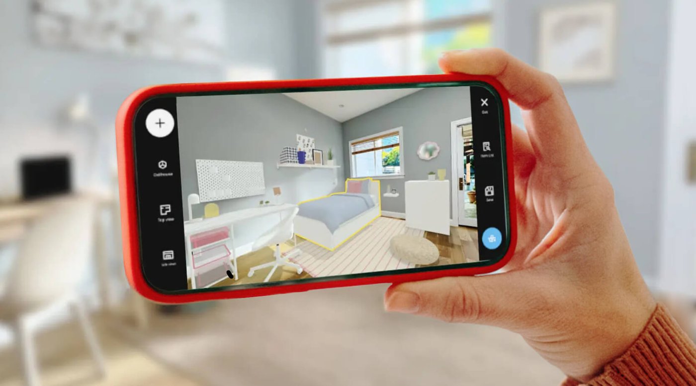 A hand holding a mobile device showing a scanned room with added IKEA dorm decor and furniture in IKEA Kreativ. The actual room is partially visible in the background.